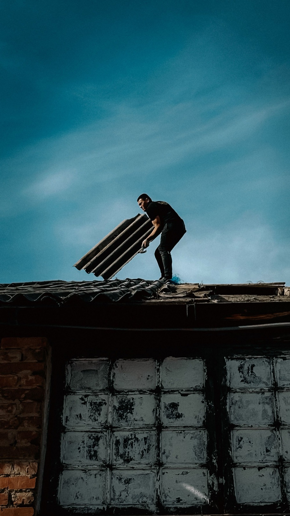 Worker carrying roofing sheets at dusk
