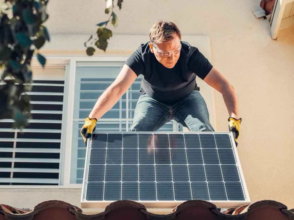 Installer lifting a solar panel onto a tiled roof